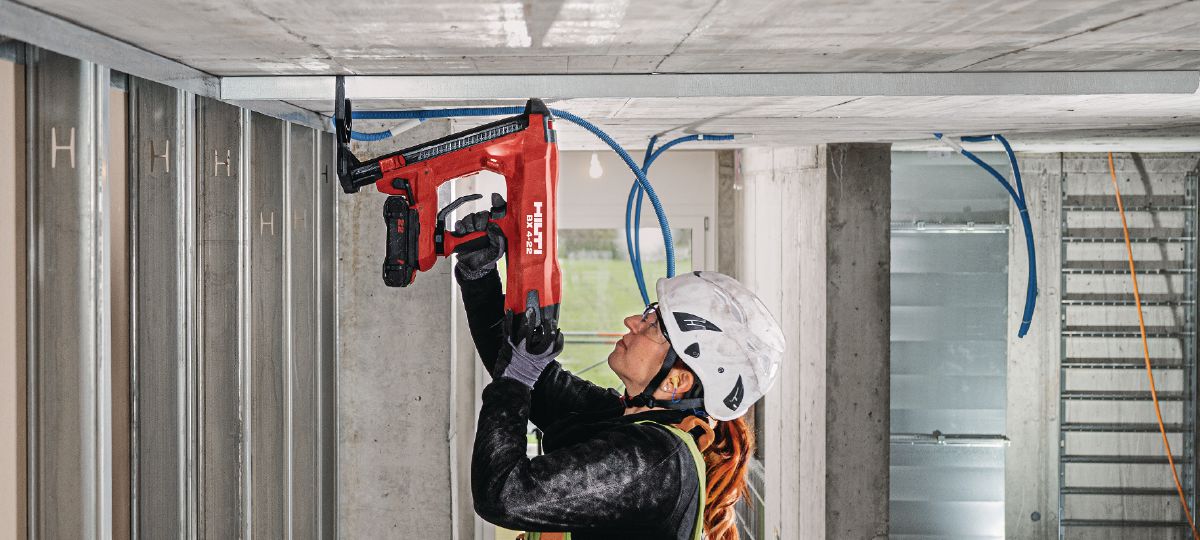 Cropped application picture of a construction worker doing a roof overhead application using the BX 4-22 with support leg mounted and the B22-85 battery