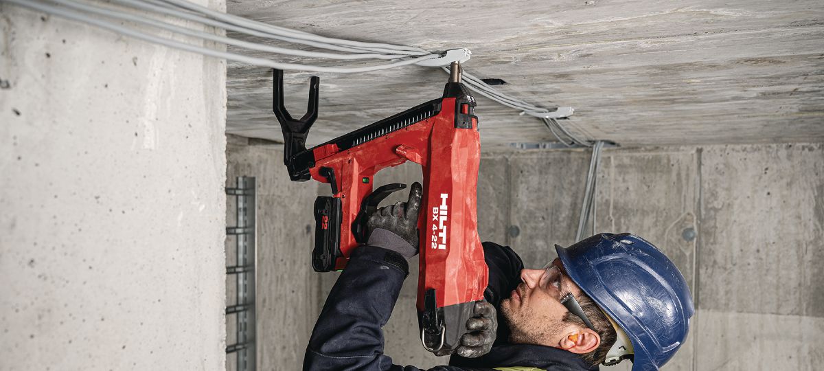 Cropped application picture of a construction worker doing a roof overhead application using the BX 4-22 with support leg mounted and the B22-85 battery to install the cable clasp X-EKB