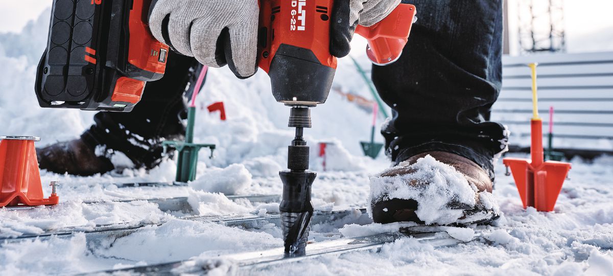 Cropped application image of Construction worker using an SID 6-22 + KCM-MD Kwik Cast combo bit to install KCCM-MD S anchors on a snowy metal deck jobsite. Golden, CO. 2024.
